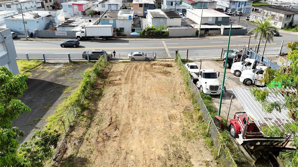 An elevated view of a cleared, rectangular dirt lot bordered by fences and parked trucks — AVE ORQUIDEA URB VALENCIA, BAYAMON, PR