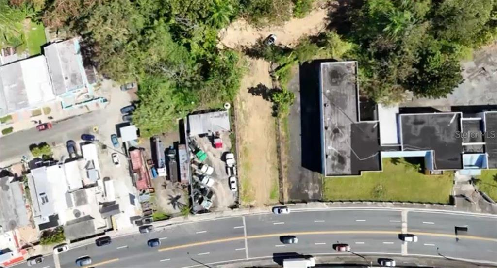 An aerial view shows a vacant dirt lot situated between two commercial buildings and a road — AVE ORQUIDEA URB VALENCIA, BAYAMON, PR
