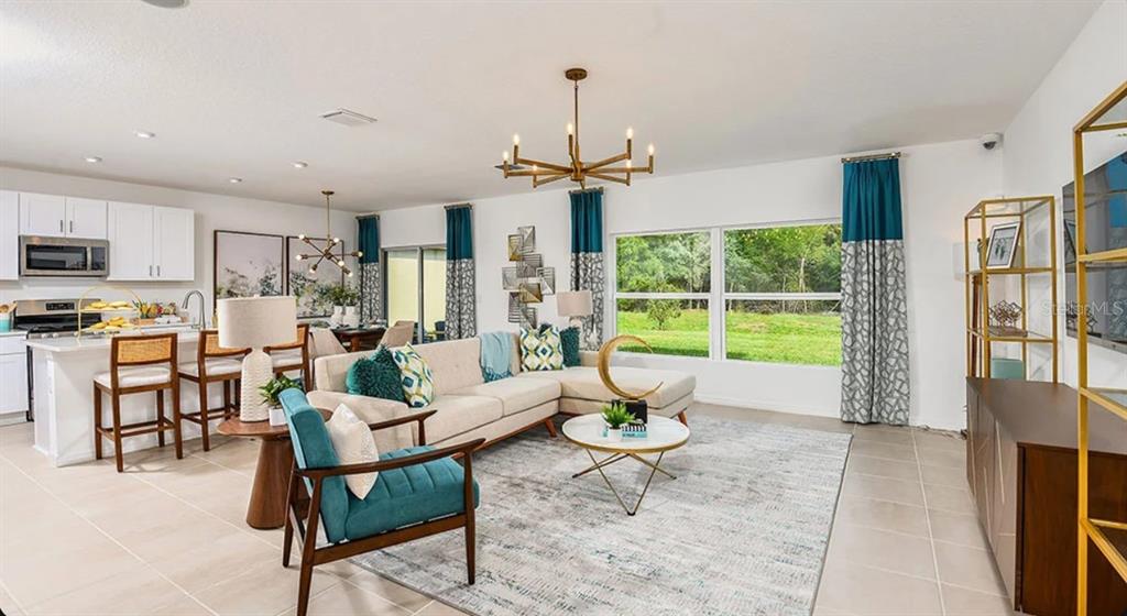 An open-concept living room and kitchen featuring a sectional sofa, teal accents, and large windows — 13819 SHELLMORE AVENUE, PALMETTO, FL