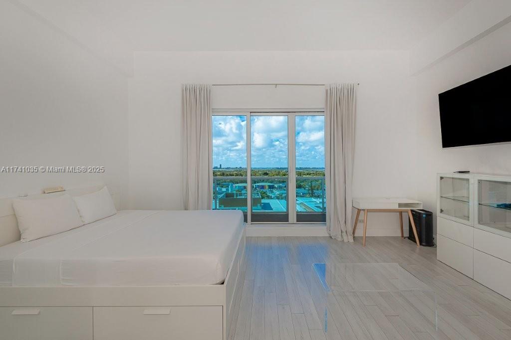 A bedroom features a white bed, a desk, a glass table, and a balcony view — 2301 Collins Ave # 1629, Miami Beach FL 33139, MIAMI BEACH, FL
