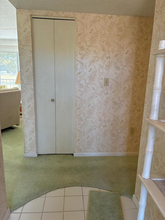 A hallway with patterned wallpaper, green carpeting, a white bi-fold closet door, and tiled flooring — 7020 COGNAC DRIVE UNIT 4, NEW PORT RICHEY, FL