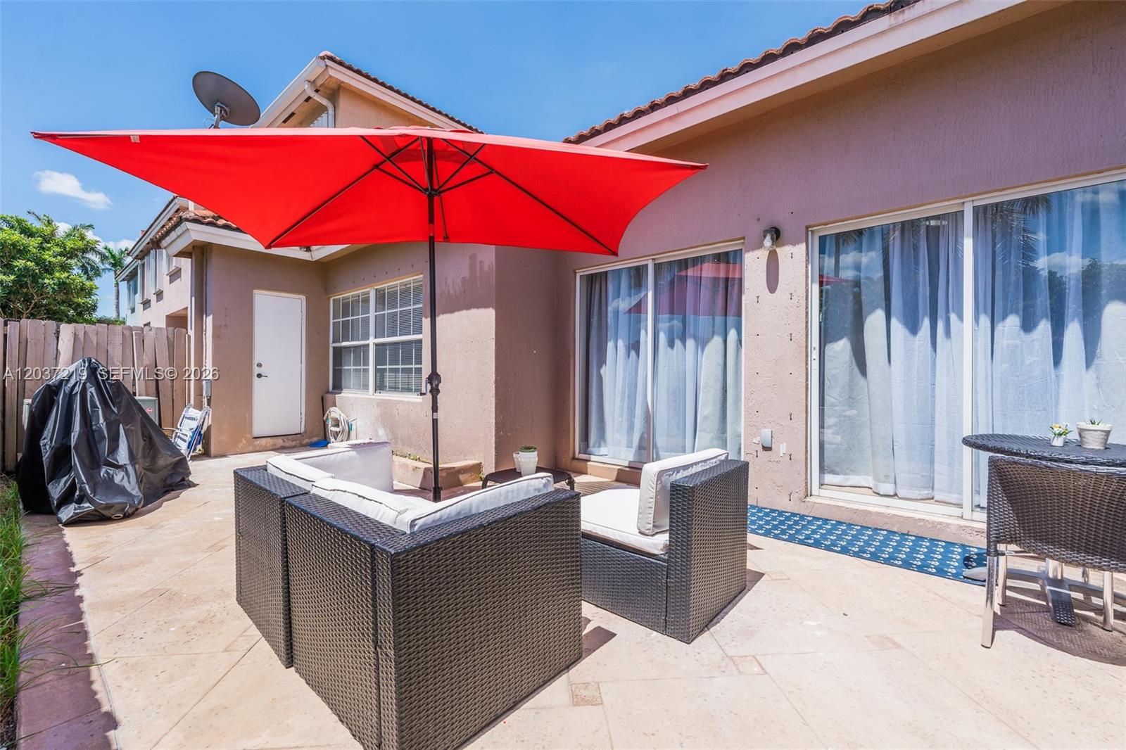 A patio features a red umbrella, wicker furniture, and sliding glass doors against a house — 10297 SW 162nd Ct, Miami FL 33196, MIAMI, FL