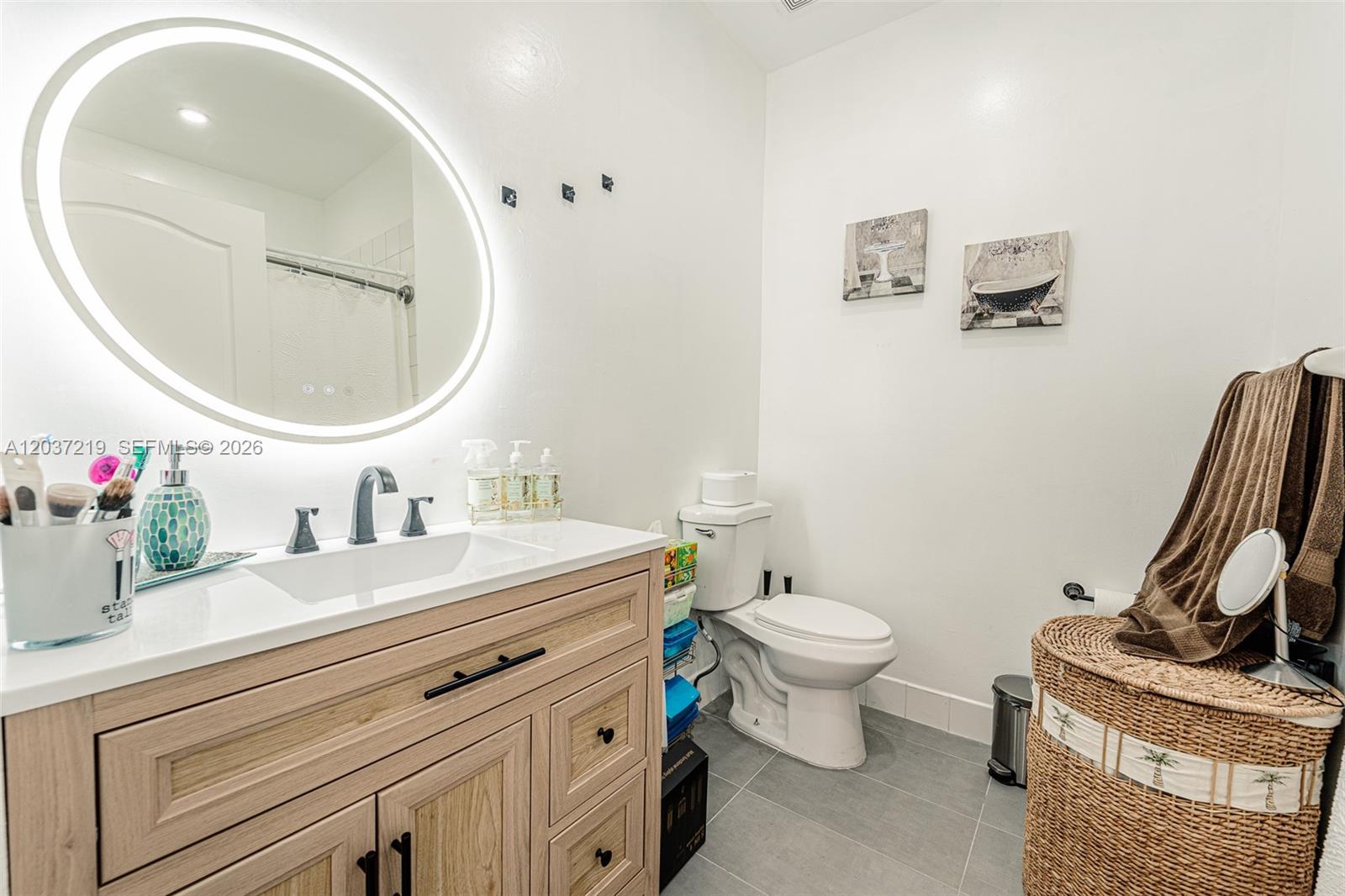 A bathroom features a light wood vanity, an illuminated oval mirror, and a white toilet — 10297 SW 162nd Ct, Miami FL 33196, MIAMI, FL