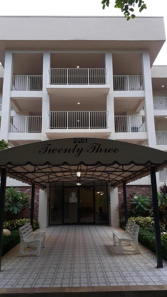The exterior of a multi-story apartment building features a covered entrance with two benches — 2601 S Course Drive # 203, Pompano Beach FL 33069, POMPANO BEACH, FL
