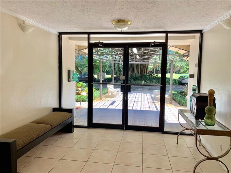 A tiled entryway features a long bench, a glass console table, and glass double doors — 2601 S Course Drive # 203, Pompano Beach FL 33069, POMPANO BEACH, FL