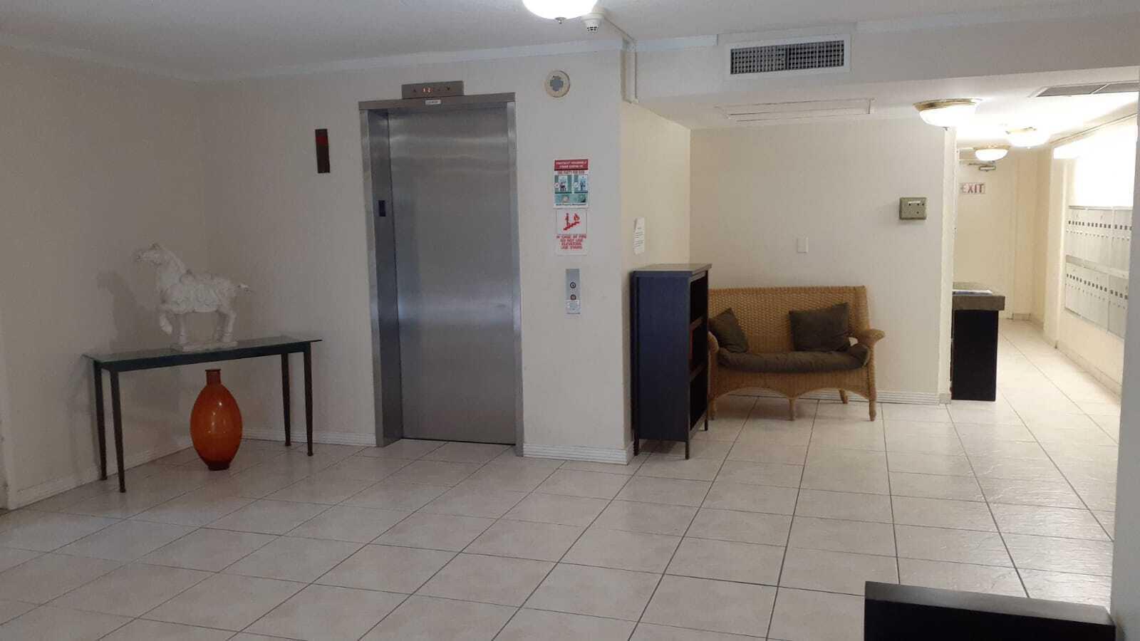 A lobby area features a stainless steel elevator, a wicker loveseat, and tiled flooring — 2601 S Course Drive # 203, Pompano Beach FL 33069, POMPANO BEACH, FL