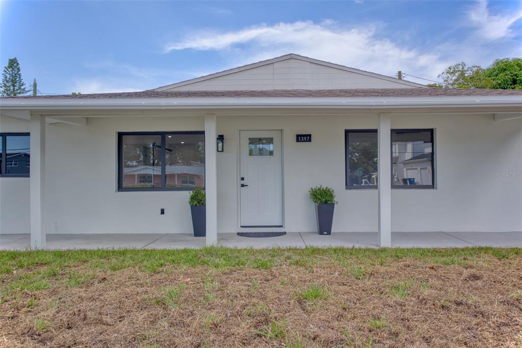 The exterior of a single-story house features a white facade, dark-framed windows, and a porch — 1397 83RD AVENUE N, ST PETERSBURG, FL