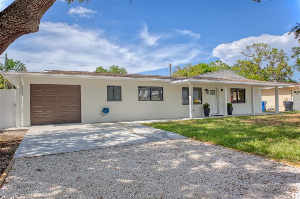A single-story house with a white exterior, brown garage door, and a gravel driveway — 1397 83RD AVENUE N, ST PETERSBURG, FL