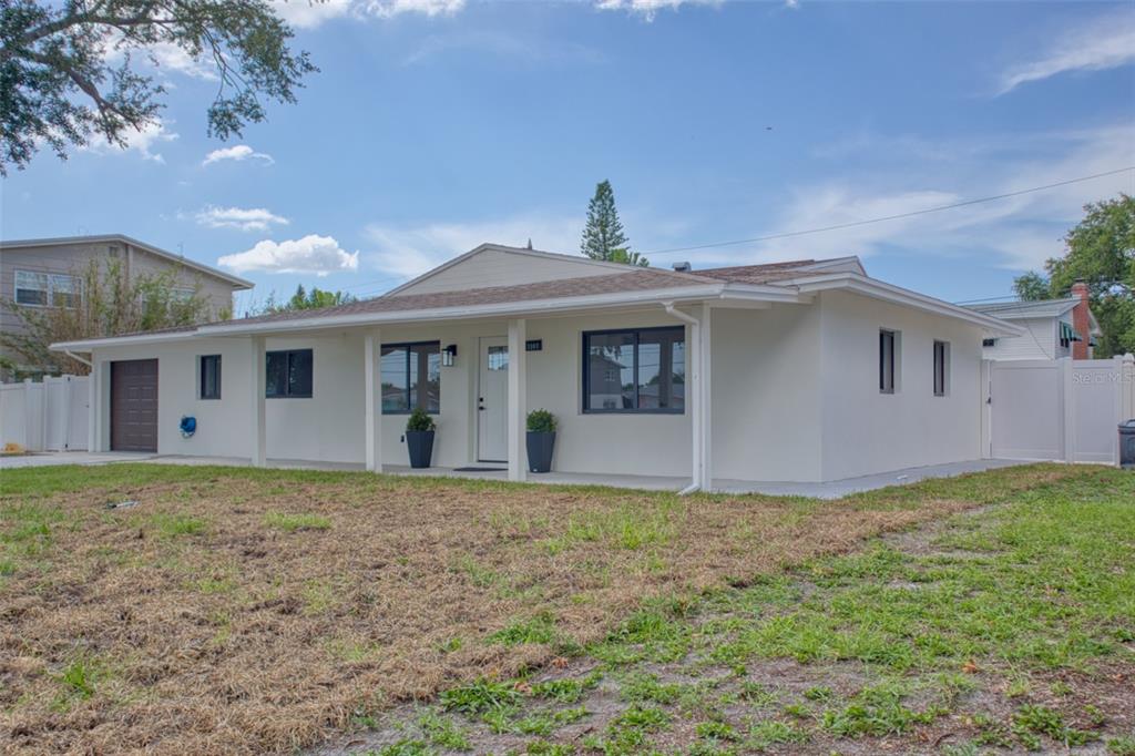 A single-story white house with a covered front porch and a dark brown garage door — 1397 83RD AVENUE N, ST PETERSBURG, FL