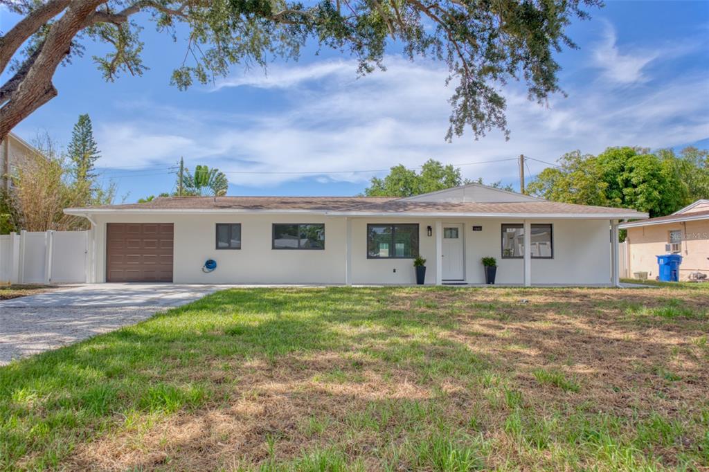A single-story house with a white exterior, a brown garage door, and a front porch — 1397 83RD AVENUE N, ST PETERSBURG, FL