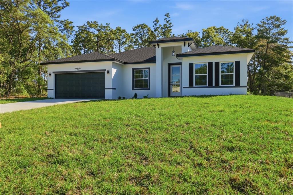 A single-story white house with a dark garage door and black shutters sits on grass — 9319 N CORTLANDT DRIVE, CITRUS SPRINGS, FL