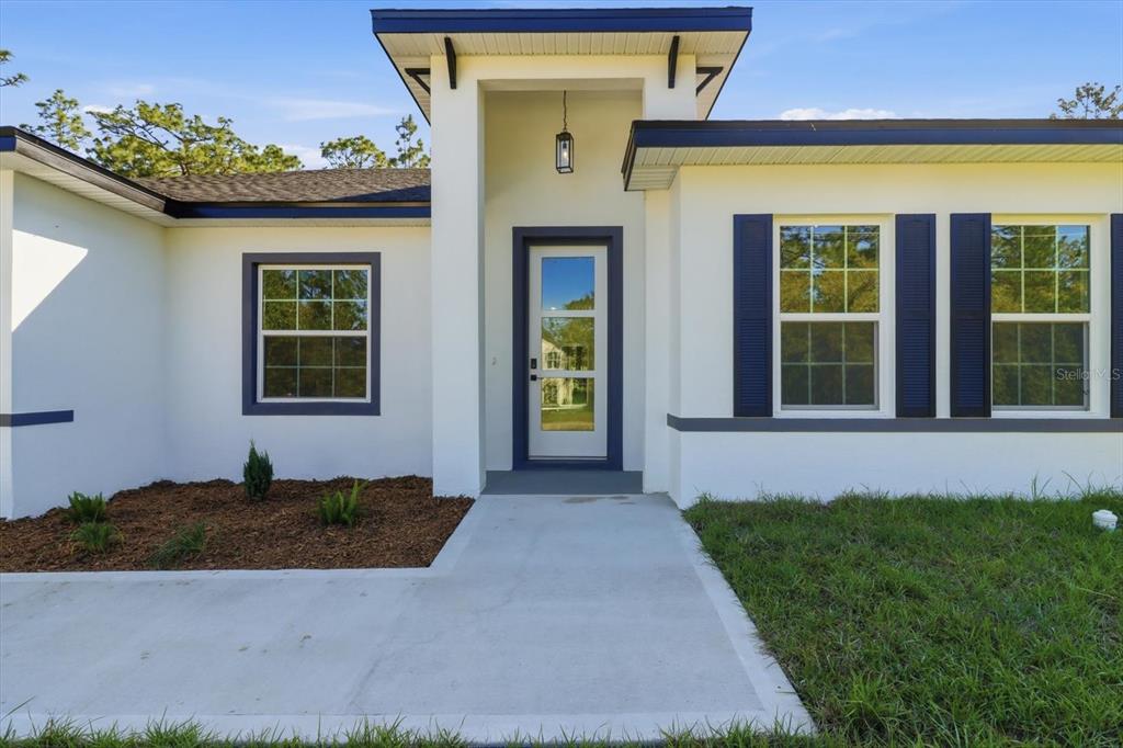 A white house exterior features a central entryway with a glass door and dark shutters — 9319 N CORTLANDT DRIVE, CITRUS SPRINGS, FL