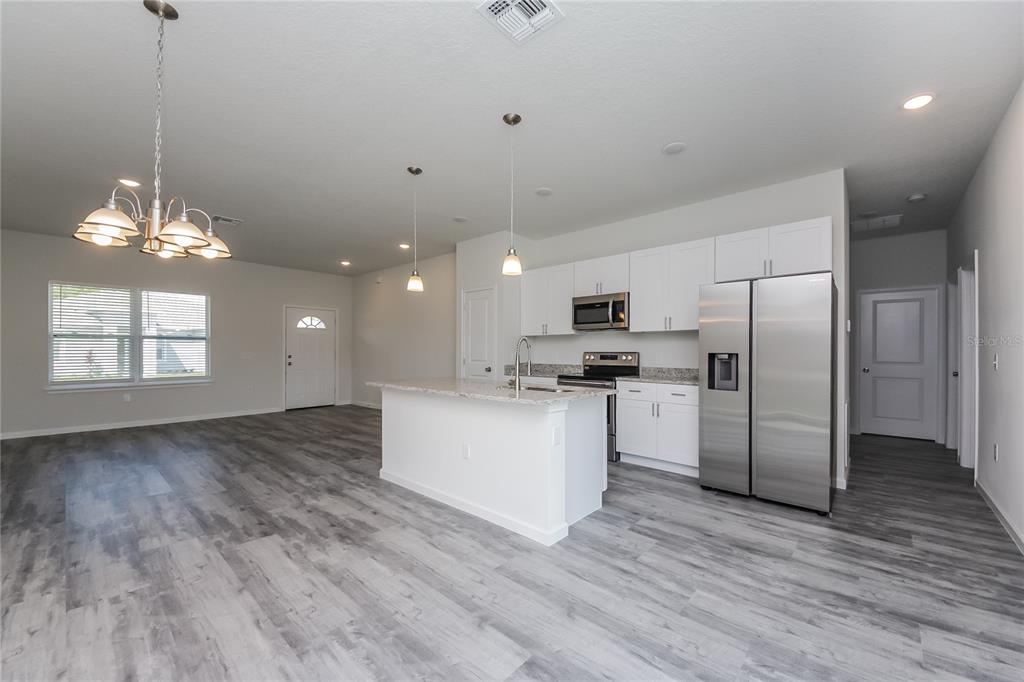 An open-concept kitchen and living area featuring white cabinets, stainless steel appliances, and gray flooring — 137 VIOLET CT, KISSIMMEE, FL