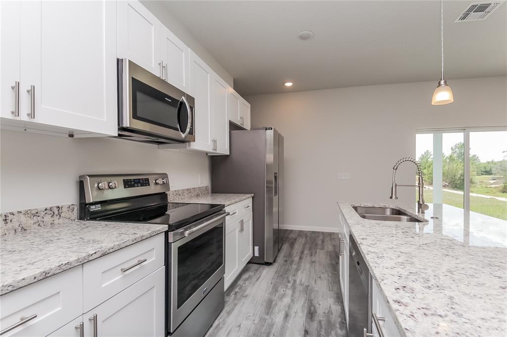 A modern kitchen features white cabinets, granite countertops, stainless steel appliances, and wood-look flooring — 137 VIOLET CT, KISSIMMEE, FL