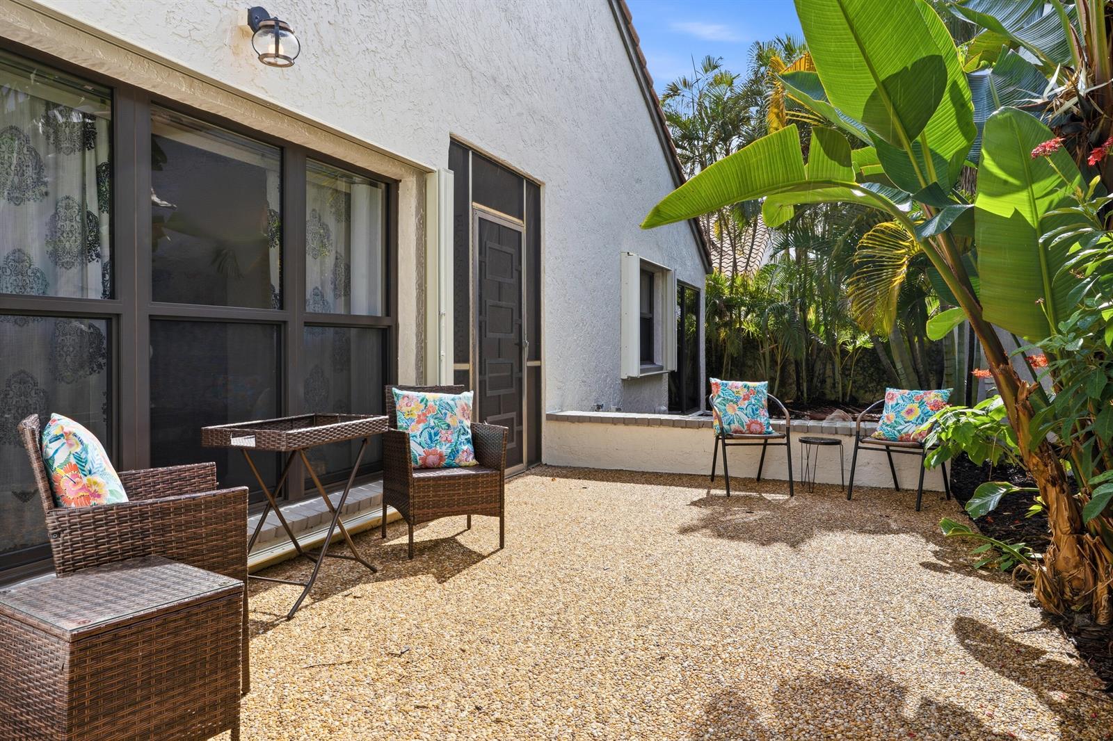 A gravel patio features wicker chairs with floral pillows and a small table near a house — 11810 Kiva Drive, Boynton Beach FL 33437, BOYNTON BEACH, FL