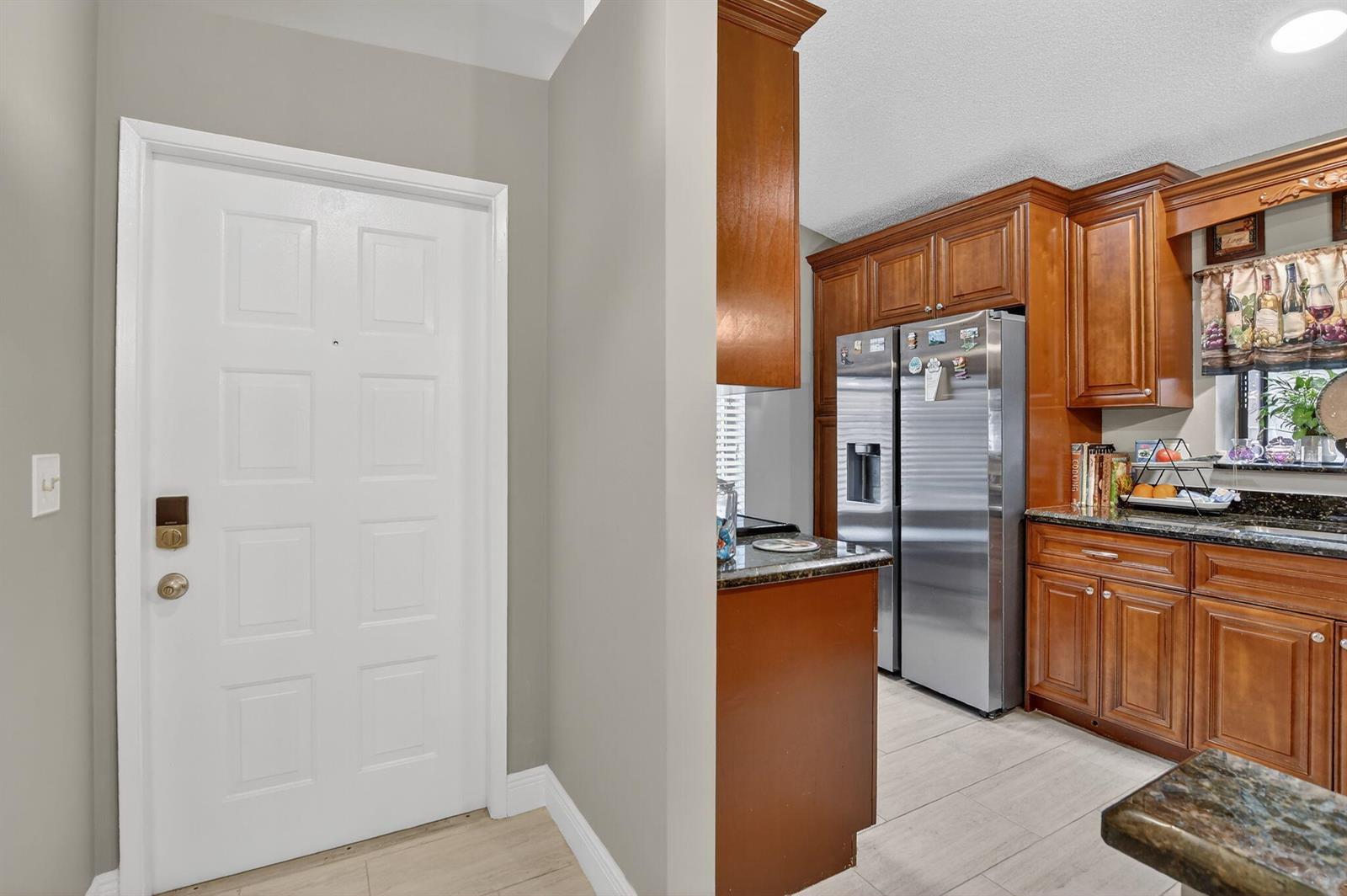 A white door stands next to a kitchen featuring wood cabinets and stainless steel appliances — 8081 Springtree Road, Boca Raton FL 33496, BOCA RATON, FL