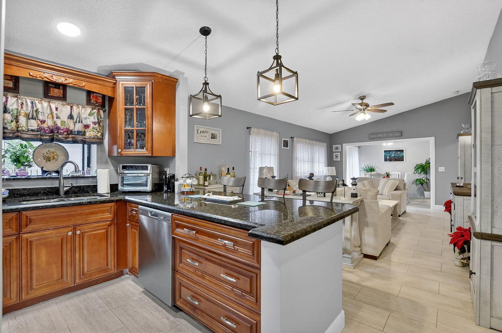 A kitchen with wood cabinets and granite countertops opens into a living area with tile flooring — 8081 Springtree Road, Boca Raton FL 33496, BOCA RATON, FL