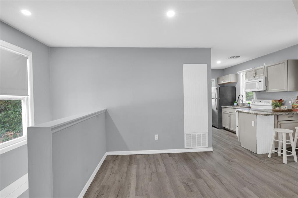A grey-walled room with wood-look flooring opens into a kitchen with light-colored cabinets — 2508 YALE AVENUE, SANFORD, FL