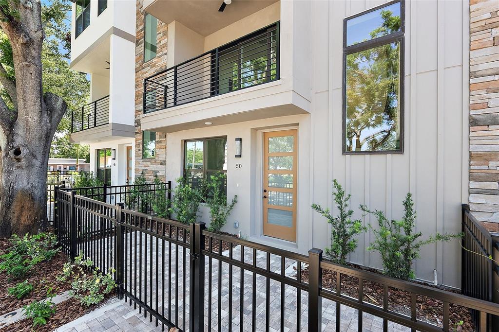 A modern multi-story townhouse exterior features a fenced patio, stone accents, and a wooden door — 50 64TH STREET S, ST PETERSBURG, FL