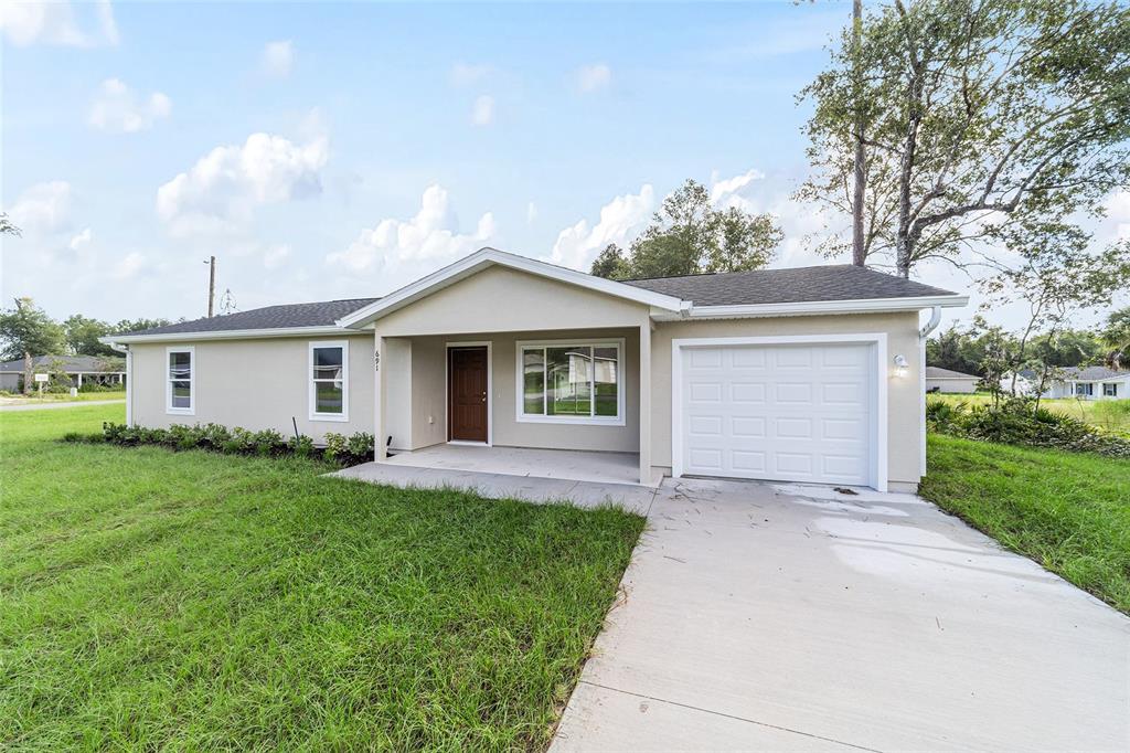 A single-story house with a beige exterior, a white garage door, and a concrete driveway — 715 NE 130TH COURT, SILVER SPRINGS, FL