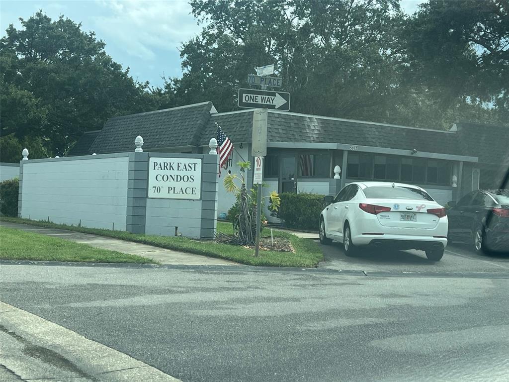 A white car is parked in front of a building labeled Park East Condos — 5100 70TH PLACE N UNIT 5100, PINELLAS PARK, FL