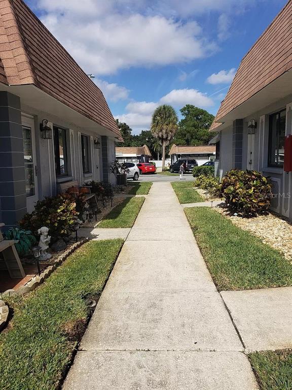 A concrete walkway leads between two residential buildings toward a street with parked cars — 5100 70TH PLACE N UNIT 5100, PINELLAS PARK, FL
