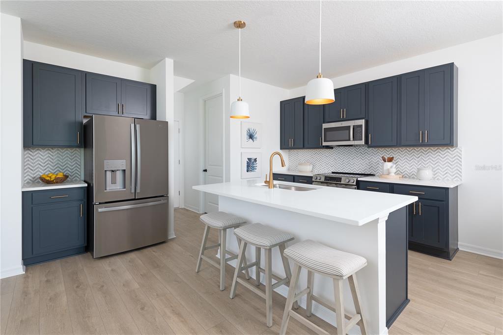 A modern kitchen features dark blue cabinets, a white island with stools, and stainless appliances — 7536 DEER VALLEY CIRCLE, TAMPA, FL