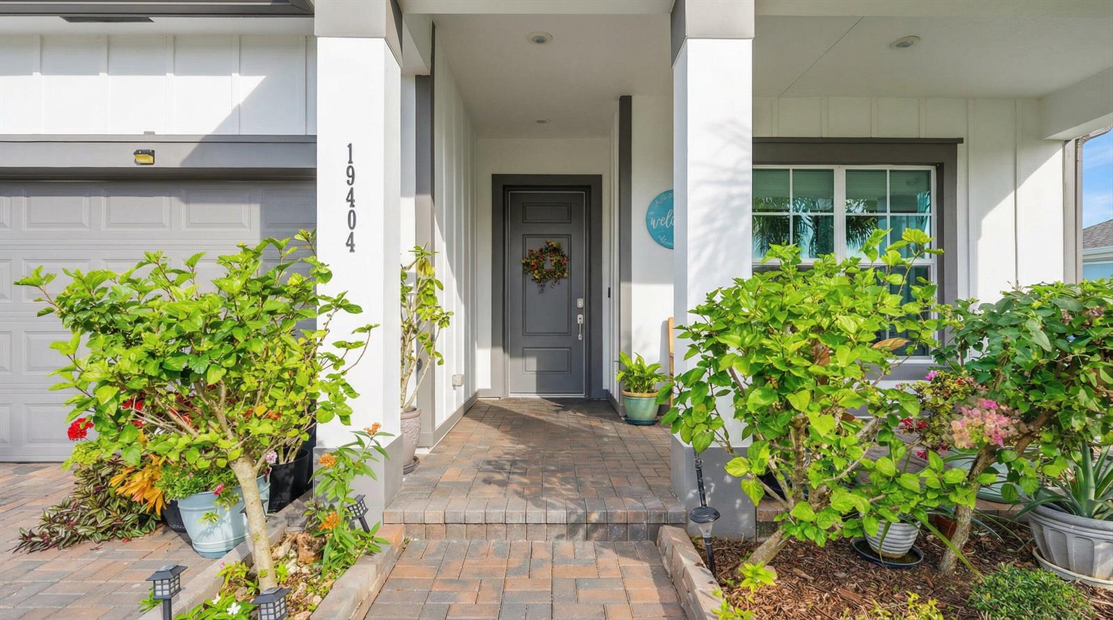 The exterior of a house features a gray front door, brick walkway, and potted plants — 19404 Broad Shore Walk, Loxahatchee FL 33470, LOXAHATCHEE, FL