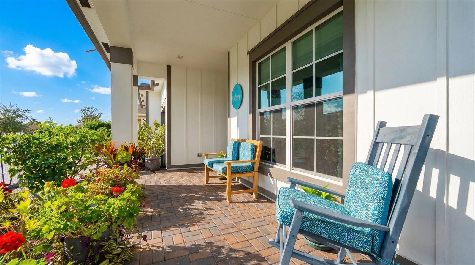 A covered brick porch features a wooden bench and a rocking chair with blue cushions — 19404 Broad Shore Walk, Loxahatchee FL 33470, LOXAHATCHEE, FL