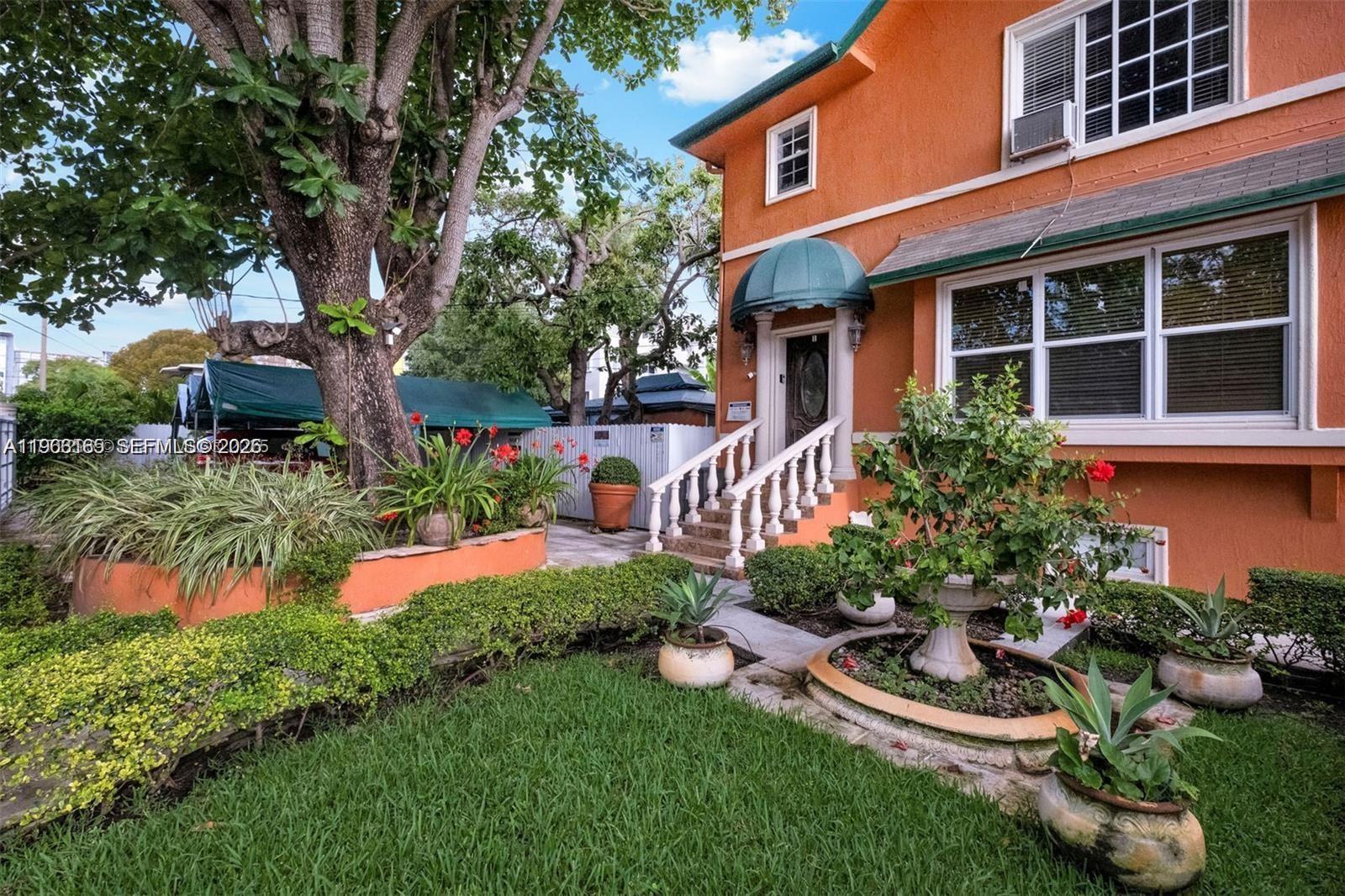 An orange house features a front porch with white railings and a landscaped front yard — 1033 NW 6th St, Miami FL 33136, MIAMI, FL