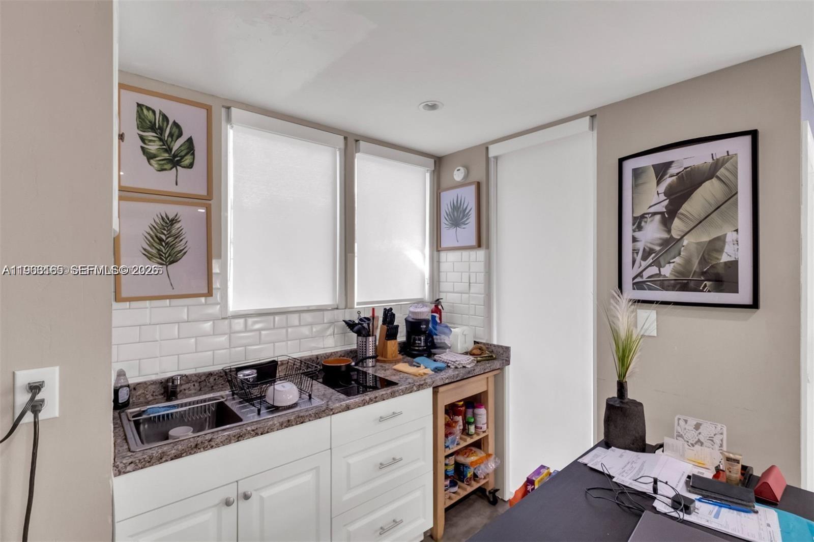 A kitchen features white cabinets, a granite countertop, subway tile backsplash, and a rolling cart — 1033 NW 6th St, Miami FL 33136, MIAMI, FL