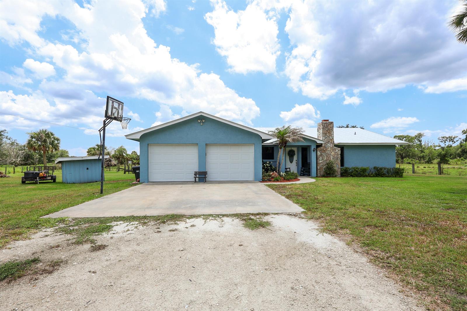 A blue single-story house with a two-car garage, stone chimney, and a gravel driveway — 860 NW 141st Street, Okeechobee FL 34972, OKEECHOBEE, FL