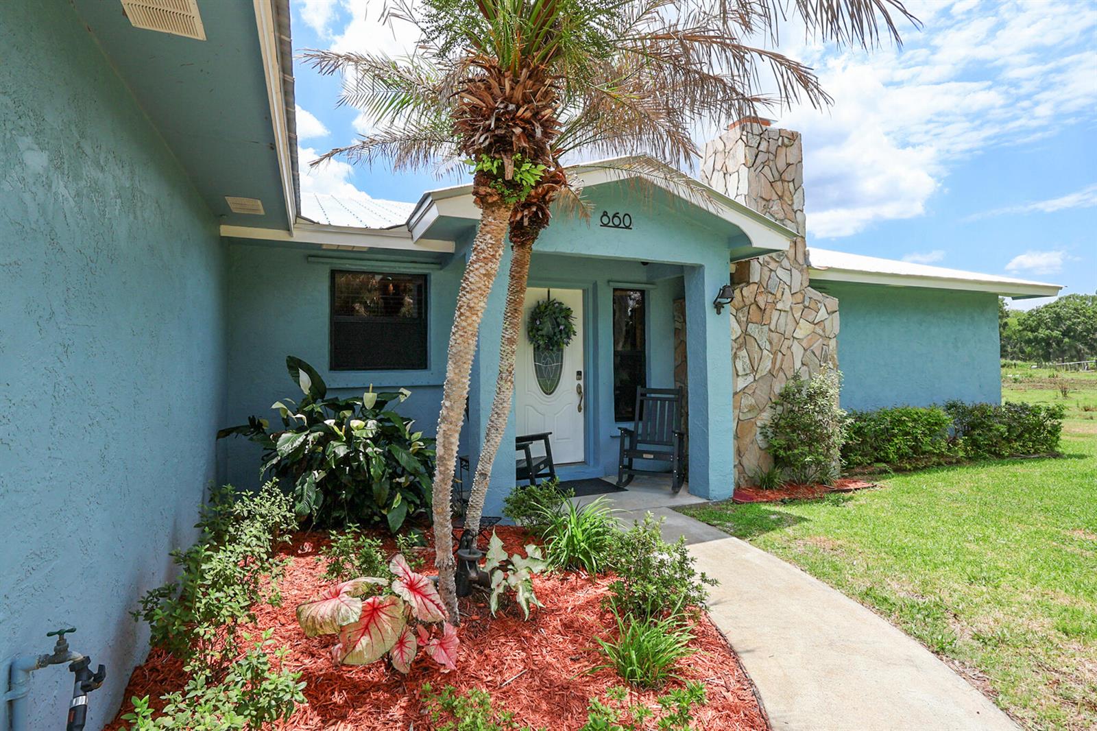 A blue house exterior features a stone chimney, a palm tree, and a front walkway — 860 NW 141st Street, Okeechobee FL 34972, OKEECHOBEE, FL