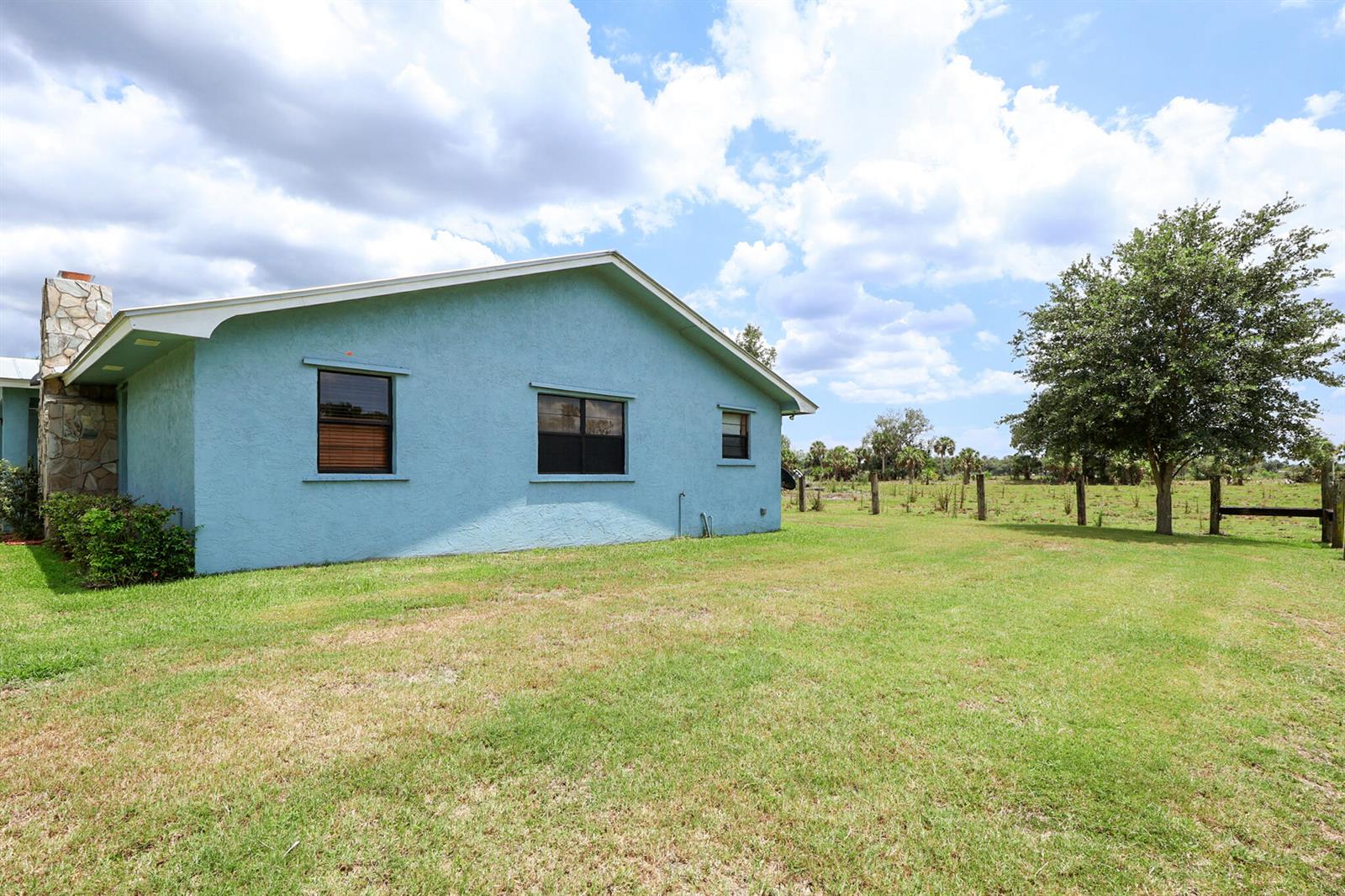 A light blue house with a stone chimney stands on a grassy lot — 860 NW 141st Street, Okeechobee FL 34972, OKEECHOBEE, FL
