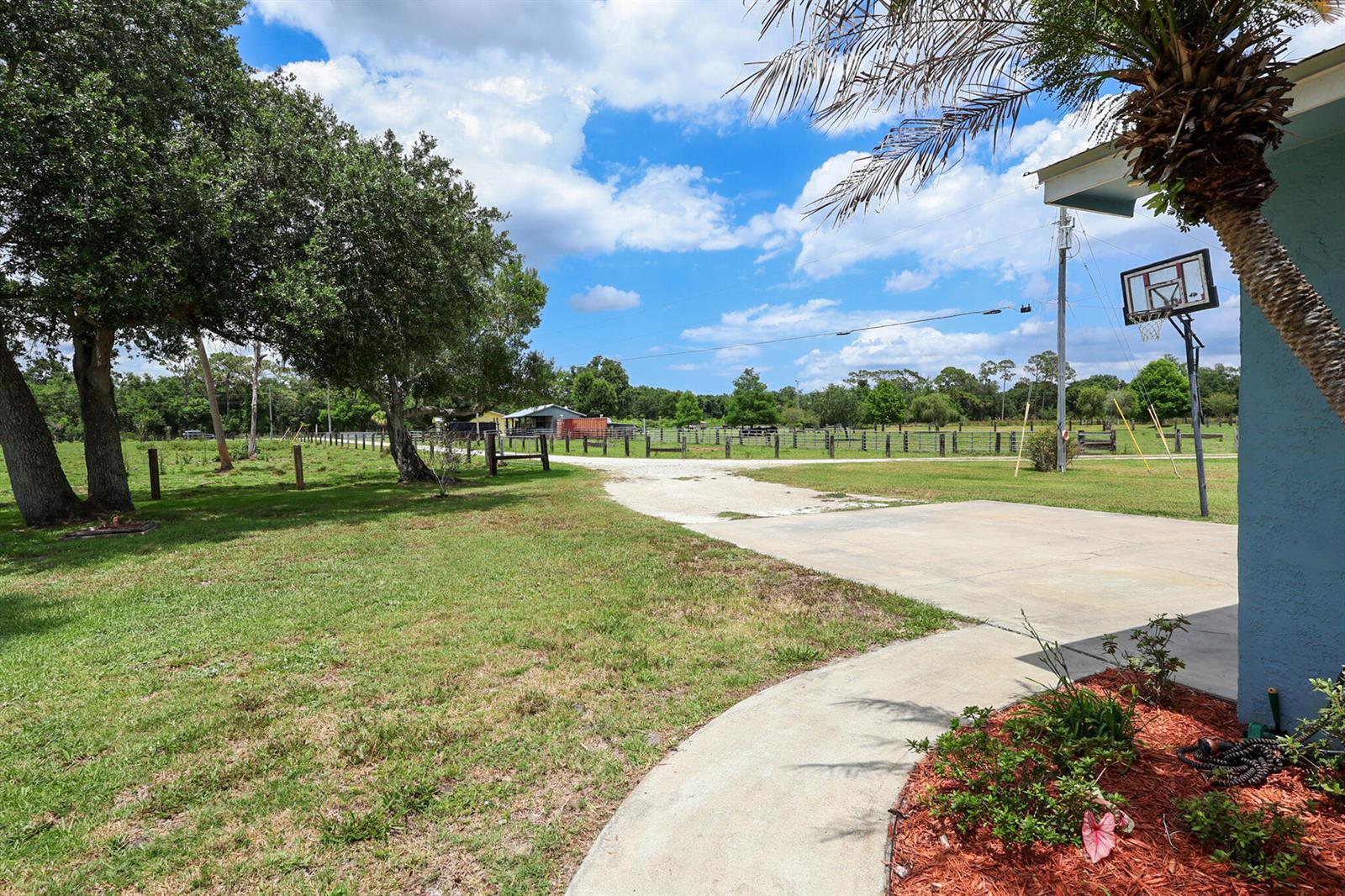 A grassy yard features a concrete driveway, a basketball hoop, and a fenced pasture — 860 NW 141st Street, Okeechobee FL 34972, OKEECHOBEE, FL