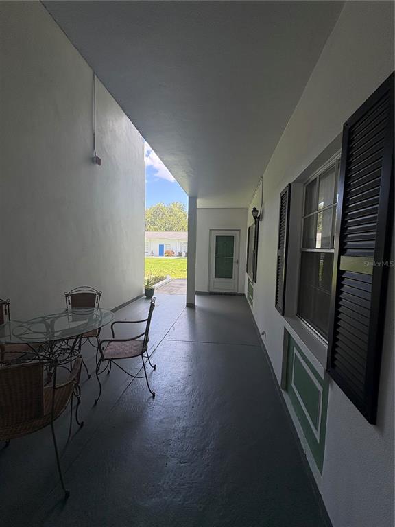 A covered patio features a glass-top table, chairs, and a view of a grassy area — 200 GLENNES LANE UNIT 114, DUNEDIN, FL