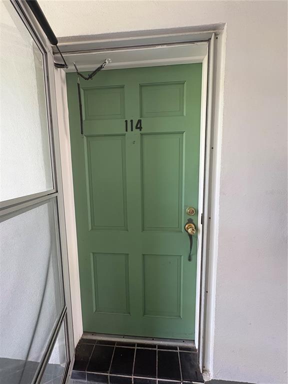 A green front door with the number 114 is set in a white exterior wall — 200 GLENNES LANE UNIT 114, DUNEDIN, FL