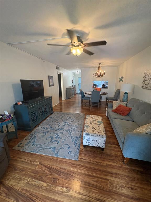 A living room with wood-look flooring, a ceiling fan, a television console, and dining area — 200 GLENNES LANE UNIT 114, DUNEDIN, FL