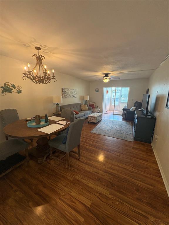 An open-concept living and dining area features wood-look flooring, a chandelier, and a sliding door — 200 GLENNES LANE UNIT 114, DUNEDIN, FL