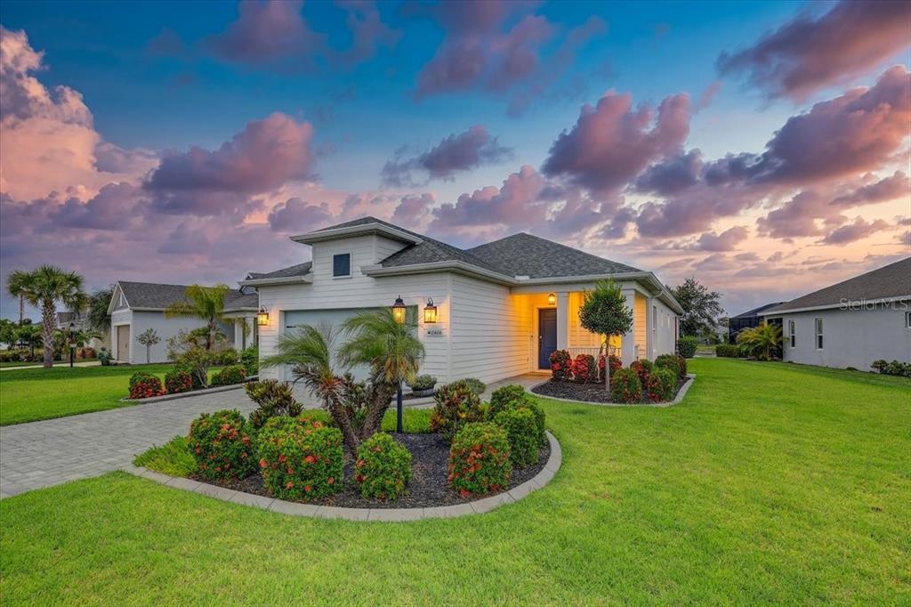 A single-story house with light siding, a paved driveway, and landscaped bushes at sunset — 10606 MORNING MARSH LANE, PARRISH, FL