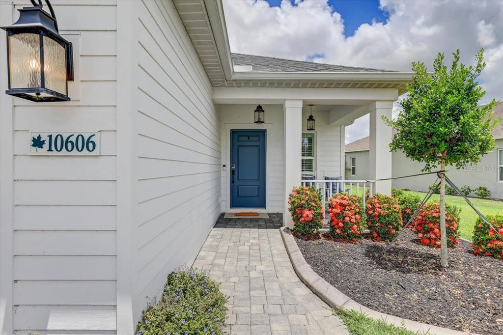 A paved walkway leads to a blue front door and a covered porch with landscaping — 10606 MORNING MARSH LANE, PARRISH, FL
