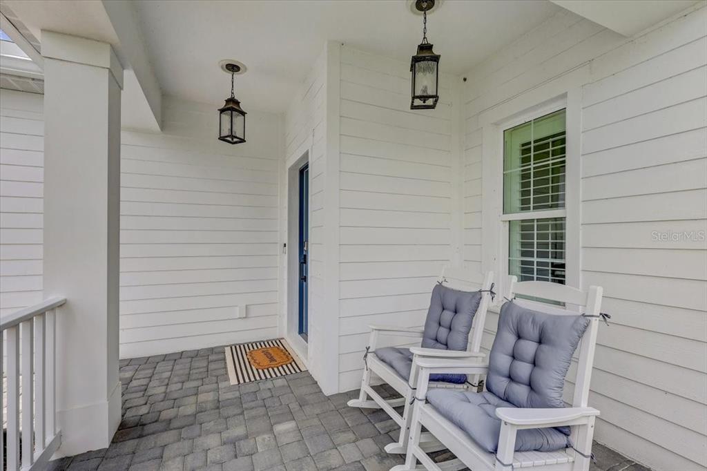 A covered front porch features white horizontal siding, two rocking chairs, and a brick floor — 10606 MORNING MARSH LANE, PARRISH, FL