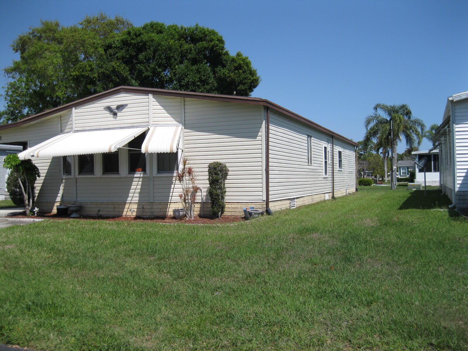 A single-story manufactured home with beige siding, a metal awning, and a grassy yard — 493 Hemingway Terrace, Fort Pierce FL 34982, FORT PIERCE, FL