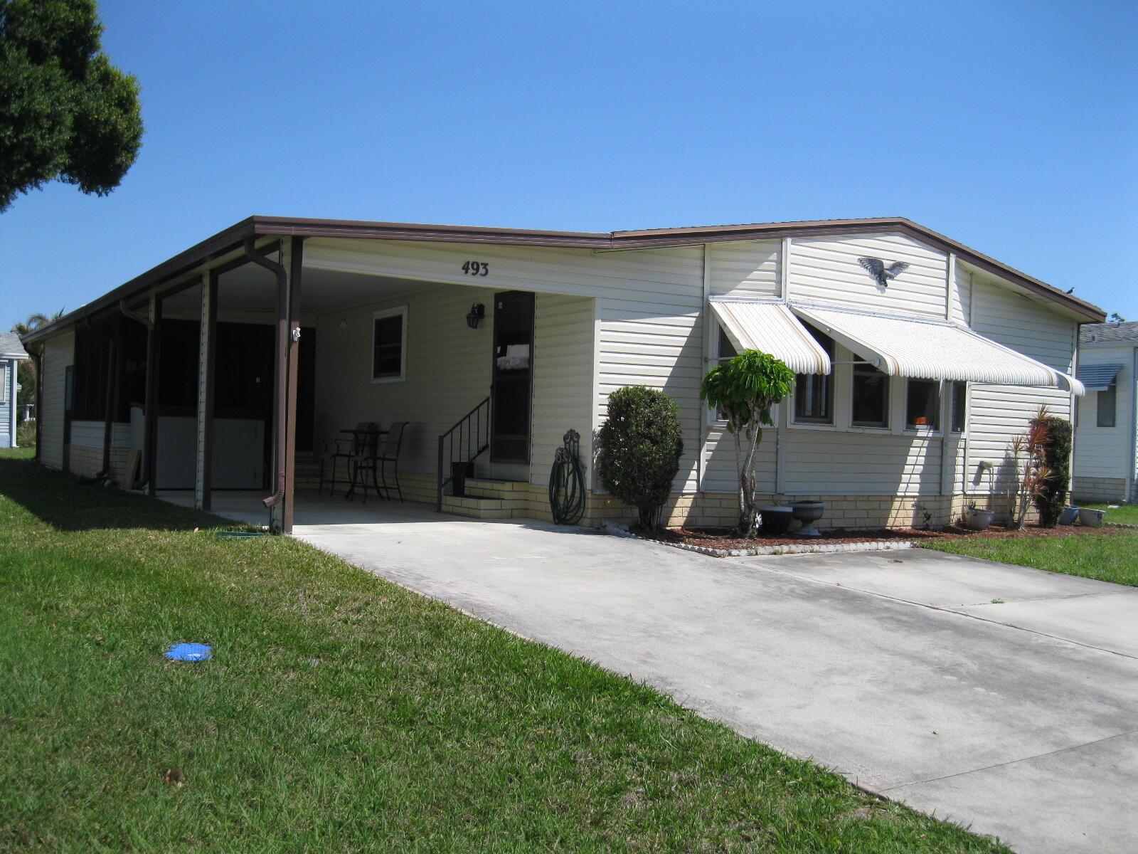 A single-story manufactured home with light siding, a carport, and striped window awnings — 493 Hemingway Terrace, Fort Pierce FL 34982, FORT PIERCE, FL
