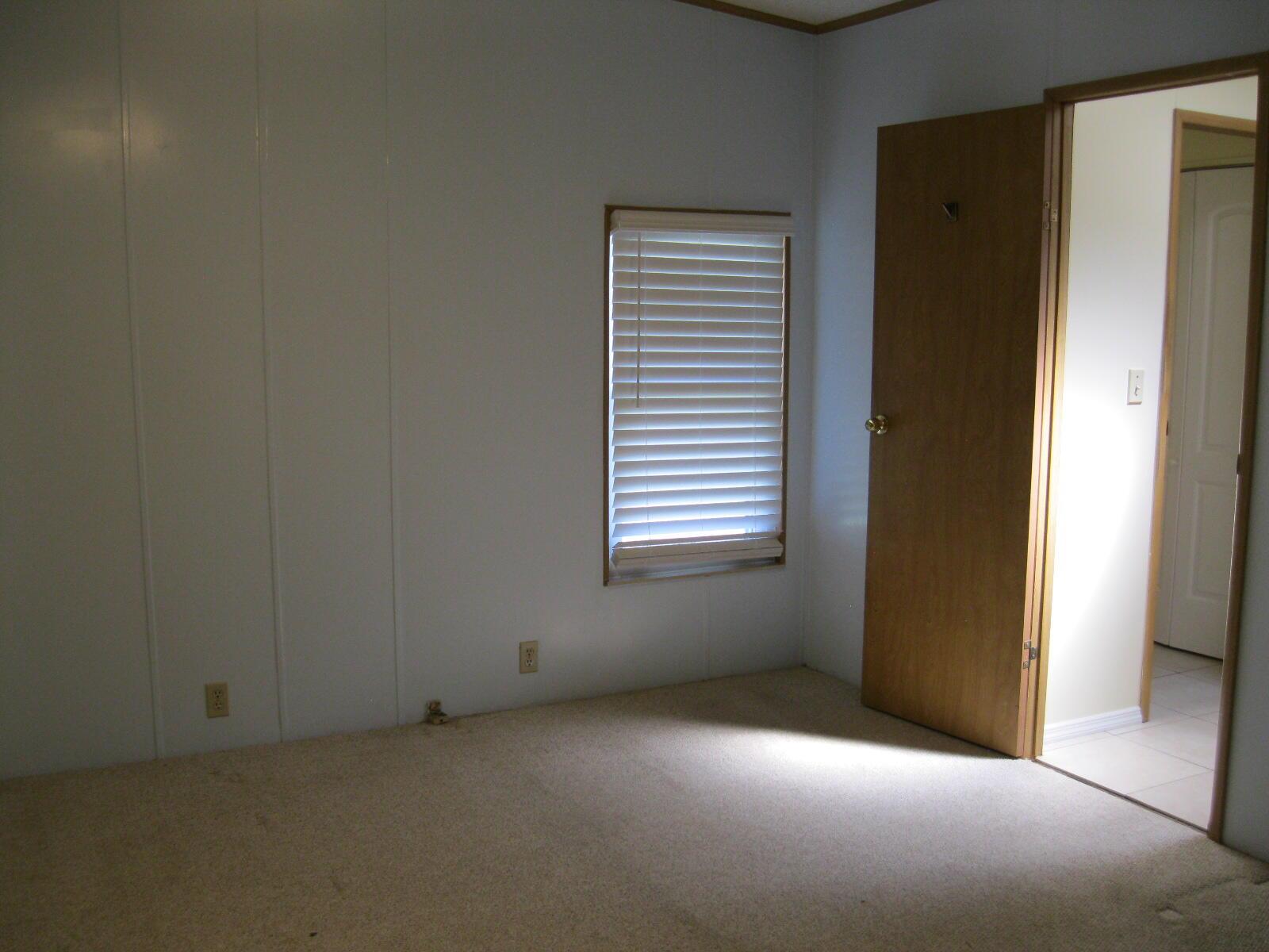 An empty bedroom with beige carpet, white paneled walls, a single window, and an open door — 493 Hemingway Terrace, Fort Pierce FL 34982, FORT PIERCE, FL