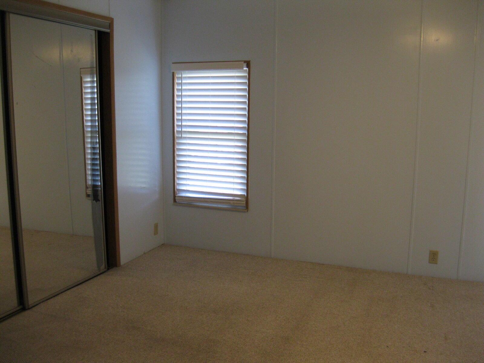 A bedroom with beige carpet, white paneled walls, a window with blinds, and mirrored closet doors — 493 Hemingway Terrace, Fort Pierce FL 34982, FORT PIERCE, FL