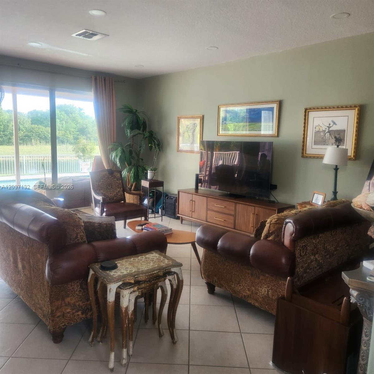 A living room features two patterned sofas, a wooden media console, and a large window — 17958 SW 36th St, Miramar FL 33029, MIRAMAR, FL