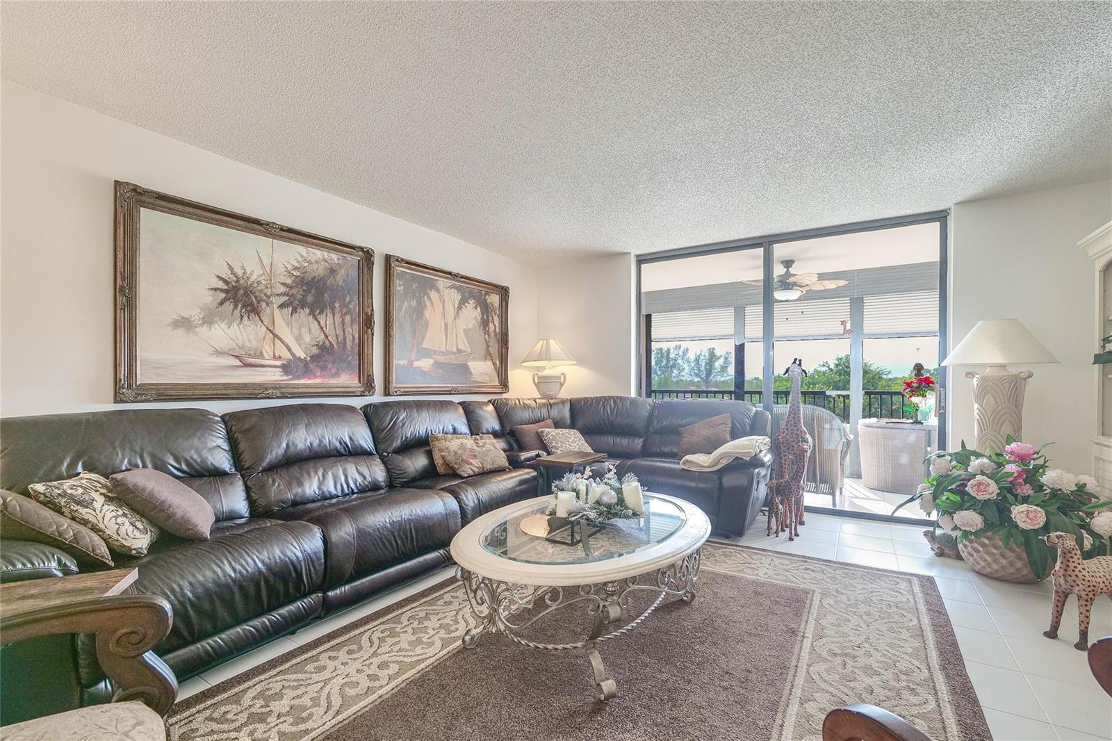 A living room features a large leather sectional, a glass coffee table, and sliding glass doors — 3591 Environ Boulevard # 401, Lauderhill FL 33319, LAUDERHILL, FL