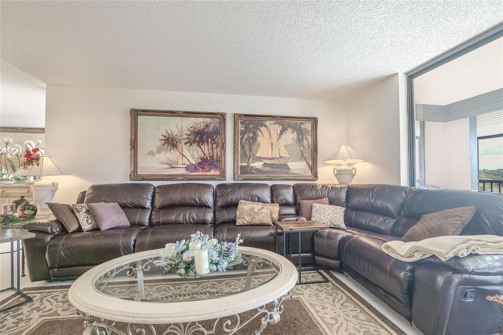 A living room features a large brown leather sectional sofa, a glass coffee table, and paintings — 3591 Environ Boulevard # 401, Lauderhill FL 33319, LAUDERHILL, FL