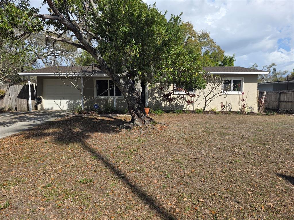 A single-story house with a tan exterior, a garage, and a large tree in front — 1015 RHODES AVENUE, SARASOTA, FL